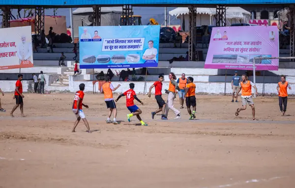 Çocuklar kumlu zeminde futbol oynuyor.