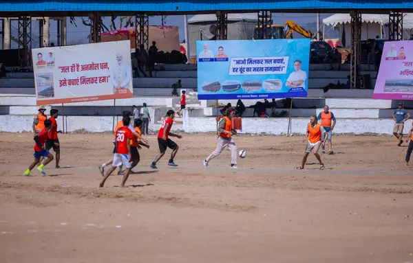 Çocuklar kumlu zeminde futbol oynuyor.