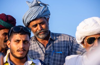Puşkar, Rajasthan, Hindistan - Kasım 09 2024: Geleneksel beyaz elbiseli bir rajasthani erkeğinin portresi çöl panayırında deve pazarında deve ticareti yaparken renkli sarıklı.