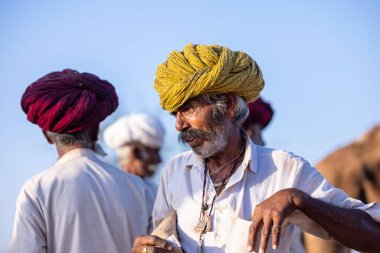 Puşkar, Rajasthan, Hindistan - 09 Kasım 2024: Çöldeki fuar alanında develerin ticareti sırasında geleneksel giysili bir Rajasthani halkının portresi.