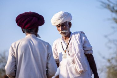 Puşkar, Rajasthan, Hindistan - 09 Kasım 2024: Çöldeki fuar alanında develerin ticareti sırasında geleneksel giysili bir Rajasthani halkının portresi.