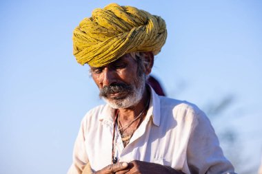 Puşkar, Rajasthan, Hindistan - 09 Kasım 2024: Çöldeki fuar alanında develerin ticareti sırasında geleneksel giysili bir Rajasthani halkının portresi.