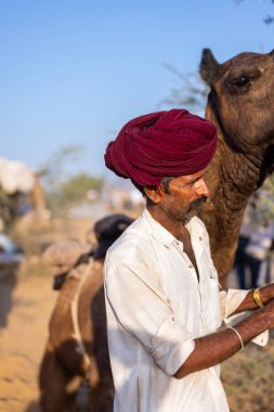 Puşkar, Rajasthan, Hindistan - 09 Kasım 2024: Çöldeki fuar alanında develerin ticareti sırasında geleneksel giysili bir Rajasthani halkının portresi.