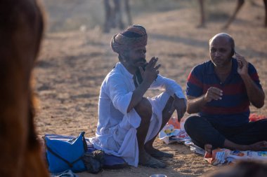 Puşkar, Rajasthan, Hindistan - 09 Kasım 2024: Çöldeki fuar alanında develerin ticareti sırasında geleneksel giysili bir Rajasthani halkının portresi.
