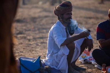 Puşkar, Rajasthan, Hindistan - 09 Kasım 2024: Çöldeki fuar alanında develerin ticareti sırasında geleneksel giysili bir Rajasthani halkının portresi.