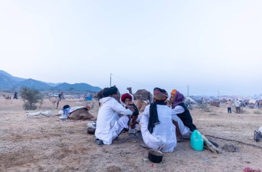 Puşkar, Rajasthan, Hindistan - Kasım 09 2024: Geleneksel beyaz elbiseli bir rajasthani erkeğinin portresi çöl panayırında deve pazarında deve ticareti yaparken renkli sarıklı.