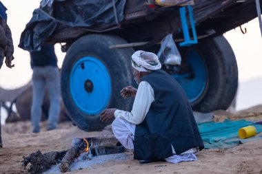 Puşkar, Rajasthan, Hindistan - 10 Kasım 2024: Geleneksel beyaz giysili rajasthani erkek portresi çöl panayırında renkli türbanlı deve fuarı sırasında develeri takas etmek için.