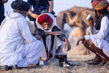 Puşkar, Rajasthan, Hindistan - 10 Kasım 2024: Geleneksel beyaz giysili rajasthani erkek portresi çöl panayırında renkli türbanlı deve fuarı sırasında develeri takas etmek için.