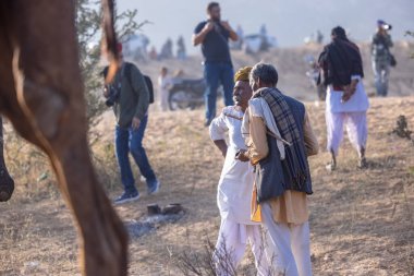 Puşkar, Rajasthan, Hindistan - 10 Kasım 2024: Geleneksel beyaz giysili rajasthani erkek portresi çöl panayırında renkli türbanlı deve fuarı sırasında develeri takas etmek için.