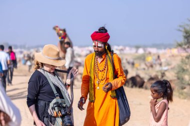 Pushkar, Rajasthan, Hindistan - 10 Kasım 2024: İtme kar deve fuarı sırasında açık zeminde renkli türbanlı kobra yılanı tutan genç yılan oynatıcısı erkek portresi.