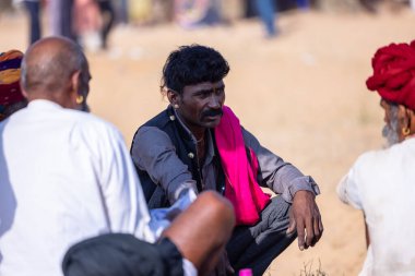 Puşkar, Rajasthan, Hindistan - 10 Kasım 2024: Geleneksel giysili rajasthani erkek portresi çöl panayırında renkli türbanlarla deve pazarında deve ticareti yaparken.