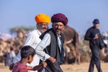 Puşkar, Rajasthan, Hindistan - 10 Kasım 2024: Geleneksel giysili rajasthani erkek portresi çöl panayırında renkli türbanlarla deve pazarında deve ticareti yaparken.