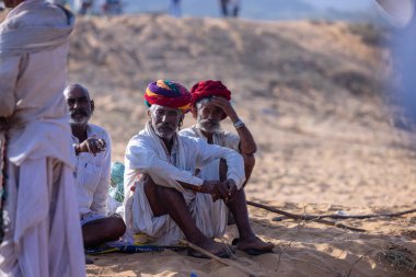Puşkar, Rajasthan, Hindistan - 10 Kasım 2024: Geleneksel giysili rajasthani erkek portresi çöl panayırında renkli türbanlarla deve pazarında deve ticareti yaparken.