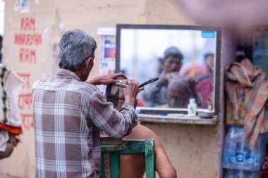 Varanasi, Uttar Pradesh, Hindistan - 20 Ocak 2024: Varanasi 'de Hindu ayinlerinin bir parçası olarak Dashashwamedh ghat' ta yaşlı bir erkeğe tıraş olan bir erkek sokak berberinin portresi.