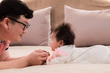 Seçici odaklı baba ve sağlıklı yeni doğmuş bebek üç ay yatakta göz teması, mutlu baba evde kızıyla konuşarak zaman geçirdi. Küçük bebek tek başına yatar. Babaya bak. Başını kaldır..