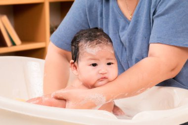 Asyalı yeni doğmuş bebek küvette duş alıyor sabun köpüğüyle dolu bir duş alıyor, bekar anne kızını yıkıyor ve bebek kafasını sıcak suyla dikkatlice ve sevgiyle yıkıyor, hijyen kavramı..