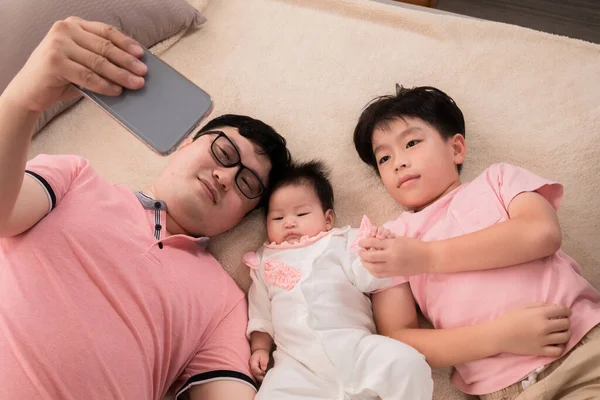 stock image Happy Asian father with kids takes photo selfie on bed. Dad, newborn baby, and son have fun spending time together on holiday, video call to mother. Healthy Happy Family with toddler infant 3 months.