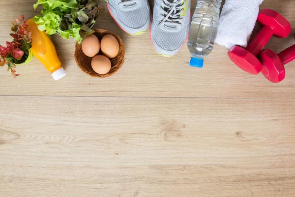 Healthy lifestyles, food, salad, eggs, orange juice and fitness equipments, sneakers, dumbbells, bottle of water, and towel in gym wooden floor background, top view flat ray with copy space