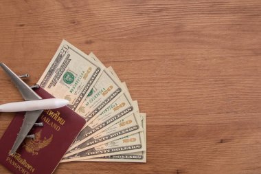 Tahta zemin üzerinde döviz ve uçak banknotları bulunan Tayland pasaportu, seyahat konsepti.