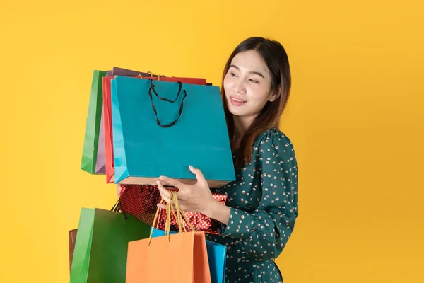 Beautiful young Asian woman excited with discount products on sale happy shopping many bags, portrait young attractive lady hold many colorful bags yellow background in studio, woman shopping concept