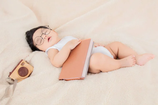 亚洲新生儿戴着眼镜 带着一本米色毛毯的书 3个月大的婴儿躺在床上休息 吃饱了以后 可爱的婴儿休息了 小屁孩小可爱睡个好觉 — 图库照片