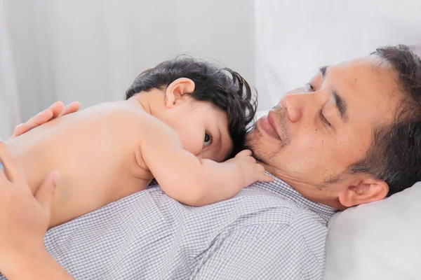 Selective focus Healthy asian father lying on bed with newborn baby. Adorable infant lying on daddy chest with safe and love. Dad and toddler have fun enjoy lying down together in holiday.