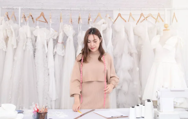 Young beautiful Asian business owner women happy working in wedding boutique showroom , Attractive dressmaker concentrate design wedding dress in bridal store, small business entrepreneur concept