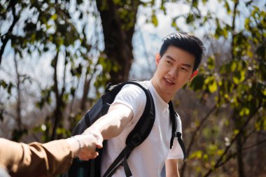 closeup man helping hand women hiking looking view beautiful nature outdoors. Asian tourists couple climbing on rock. Partner adventure hiking trail travel together in forest summer stand on peak mountain.
