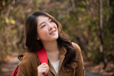 Beautiful Asian girl in jungle suit walking trail alone in the Autumn field sunlight, lifestyle adorable young woman enjoy smiling feeling freedom happy in wild forest park spent the holiday vacation in nature