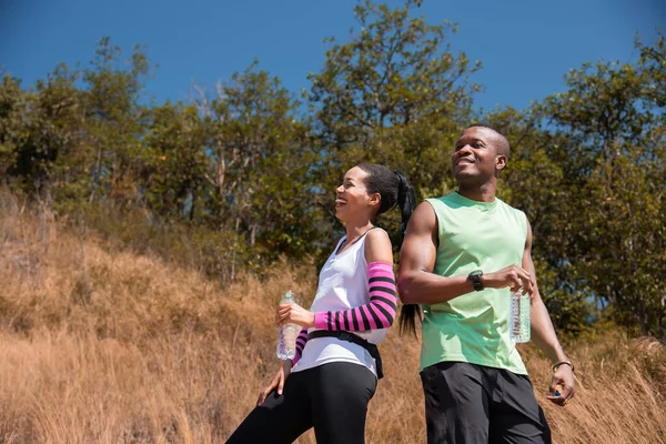 stock image Athlete couple standing drink water while running in the forest, Refresh body by drinking water. African American man and woman runner sport training together. workouts and healthy lifestyle.