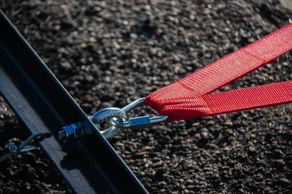 stock image A close-up view of a red strap secured with a metal clasp, emphasizing the texture and details of industrial materials. The image captures the strength and precision of the connection.