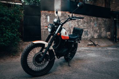 Sadece editörler kullanır. Turuncu ve beyaz renkli bir klasik Suzuki motosikleti, Ukrayna 'nın Kyiv kentinde yemyeşil ağaçlar ve yeşilliklerle çevrili sessiz bir caddeye park edilmiştir..