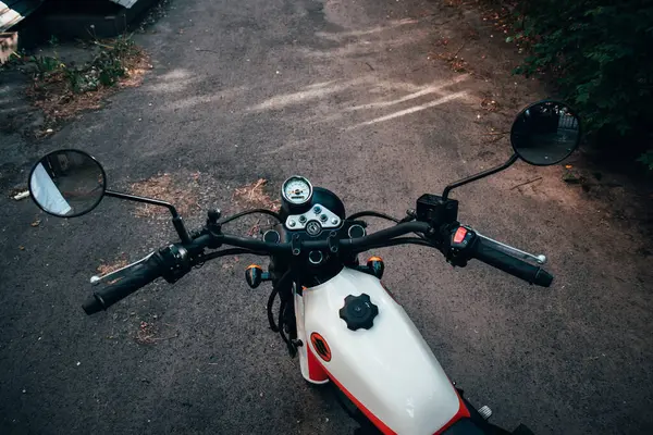 stock image Editorial use only. A vintage-style Suzuki motorcycle with an orange and white color scheme is parked on a quiet street in Kyiv, Ukraine surrounded by lush green trees and foliage.