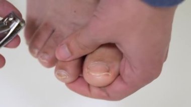 A guy cuts his toenails with pliers on white background