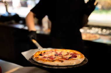 Bulanık arka planda çalışan bir şefle renkli gurme pizzaya odaklanın.