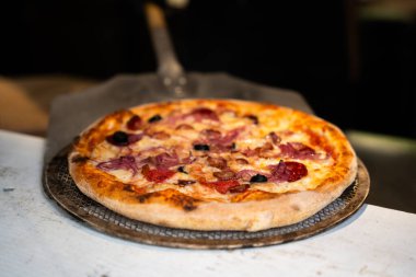 Arka planda şefin ve restoran içinin olduğu yeni pişmiş bir pizzanın yakın plan görüntüsü.