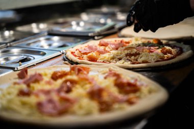 Siyah eldivenli eller pizza tabanına bol bol peynir serpiyor..