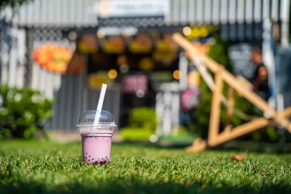 A lone cup of pink bubble tea with a straw, set against a blurred background of a vibrant street food stall.