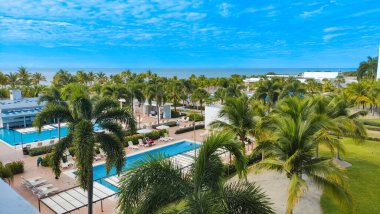 Tropik sahil oteli. Açık hava turistleri. Şatafatlı plaj kompleksi tatil köyü ve oteli. Yüzme havuzları, güneşlenme odaları ya da şemsiyelerin altında palmiye ağaçları ve mavi gökyüzü..