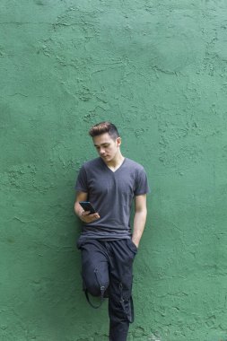 Şehirdeki yeşil duvar boyunca akıllı telefonuyla mesajlaşan genç adam.