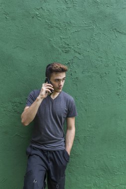 Genç bir çocuk telefonda konuşuyor. Yakışıklı adam güzel bir telefon konuşması yapıyor. Neşeli gülümseyen işadamı, yeşil arka planda tek başına dikilip akıllı telefondan konuşuyor.