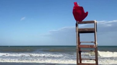 Okyanusta yüzmeyi yasaklayan kırmızı bayrak. Sahilde kırmızı bayrak sallayan boş tahta bir kurtarma sandalyesi..