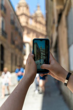 Genç turist, Salamanaca kentinin anıtlarının fotoğraflarını sosyal ağlarda paylaşmak için akıllı telefon kullanıyor. İspanya