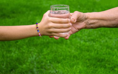 Büyükannem bir çocuğa bir bardak temiz su veriyor. Seçici odaklanma. Doğa.