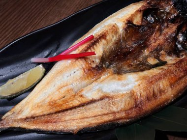 Japanese style Salted Mackerel with lemon slice on stylish table, under spot light.