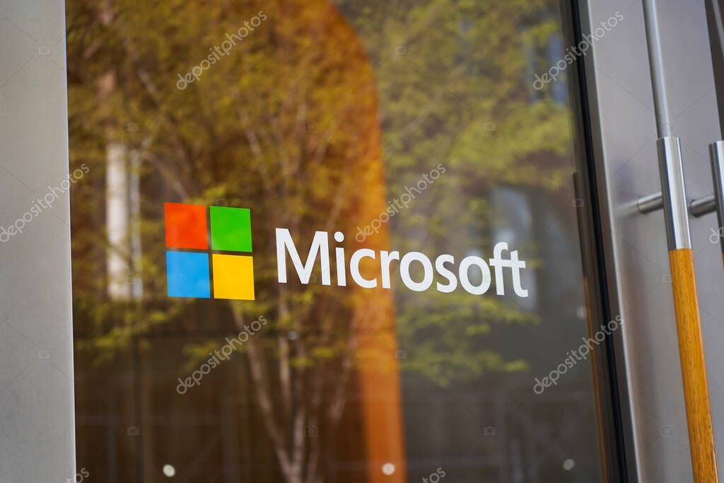 New York, NY - April 9, 2023: Microsoft logo on glass door on SoHo Manhattan shop with green tree reflection.