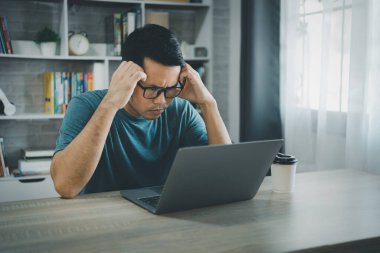 Asyalı serbest çalışan adam gözlük takıyor ve evde dizüstü bilgisayarla çalışırken stresli depresyon dönemleri geçiriyor. Depresyondaki adam evde çalışan üzgün adamlar. Herhangi bir yerde çalışma kavramı.