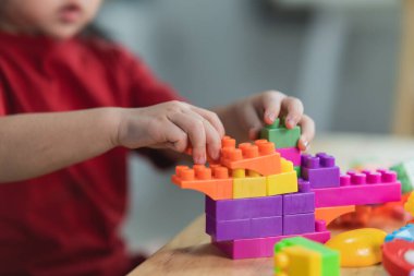 Asyalı, komik, renkli tişörtlü, lego ya da oyuncak bloklarıyla oynayan, anaokulu odasında ya da oturma odasında kule inşa eden komik anaokulu çocuğu. Çocuklar oynuyor. Kreşteki çocuklar.