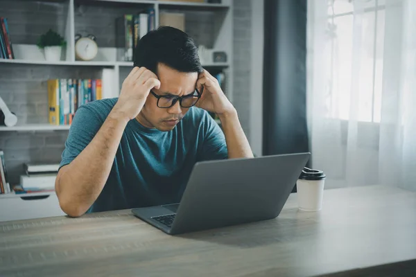 アジアのフリーランスの男性は 自宅のノートパソコンで仕事をしながら ストレスの多いうつ病悲しい時間を過ごしています うつ病の男は自宅から働く悲しいシリーズ どこにいても — ストック写真