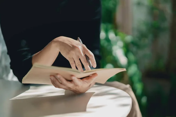 亚洲职业女性穿着黑色衬衫 在室内咖啡店桌上的小笔记本上写着日记本 女人在咖啡馆里记录和喝咖啡 从任何概念出发开展工作 — 图库照片
